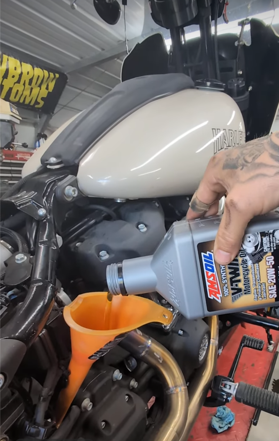 Person pouring oil into a motorcycle using a funnel and bottle labeled 'Amsoil'